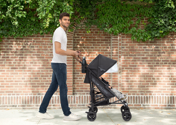 Man pushing a black stroller against a brick wall with greenery