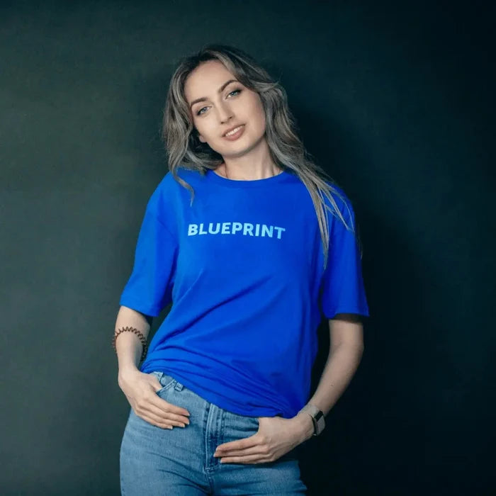 Woman wearing blue Blueprint t-shirt posing against dark background