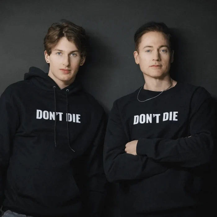Two men wearing black Don't Die hoodies against dark background