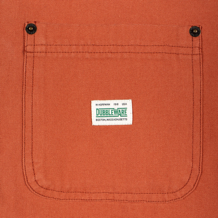 Close-up of a textured orange canvas pocket with a white Dubbleware label stitched in the center, featuring two black snap buttons at the top corners.