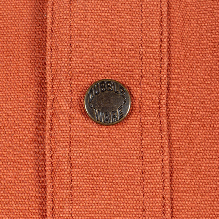Close-up of an orange woven fabric with vertical stitched channels and a round dark metal button embossed with the brand name 'DUBBLE WARE'.