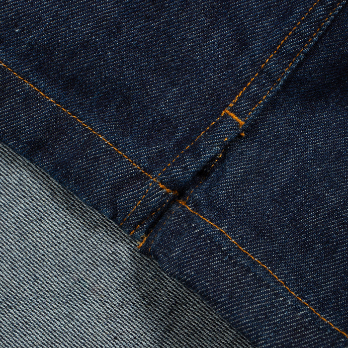 Close-up of dark indigo denim fabric with orange contrast stitching and a lighter gray denim section folded over.