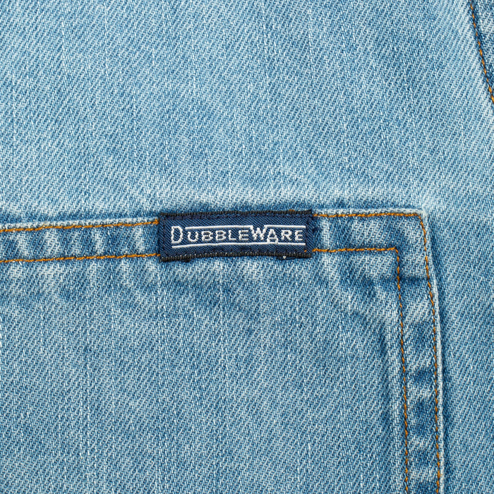 Close-up of a light blue denim garment showing a front pocket with contrast stitching and a small dark brand label reading Dubbleware.