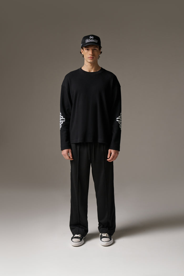 Person wearing a black outfit with white text on sleeves against a neutral background