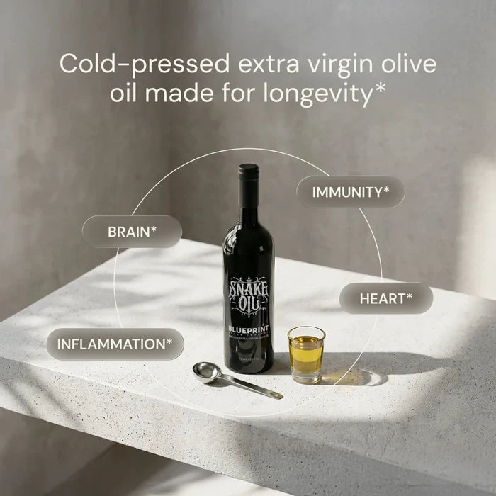 Bottle of 'Snake Oil Blueprint' olive oil with a glass on a white surface, labeled for health benefits.