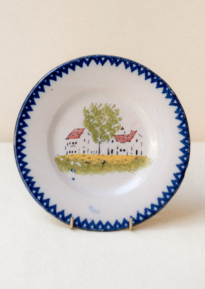 A plate with hand painted house motif and blue patterned rim.