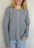 A woman wearing a heather grey cardigan with white button front.