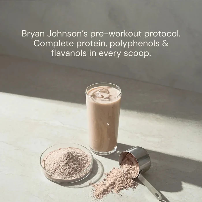 Glass of a protein shake with a scoop and container of protein powder on a light surface.