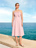 Woman in a pink dress standing by the ocean with a clear blue sky.