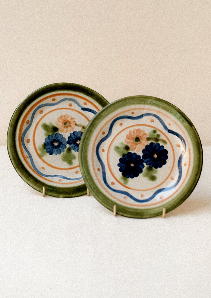 A pair of floral and squiggle painted plates in green, blue and orange.