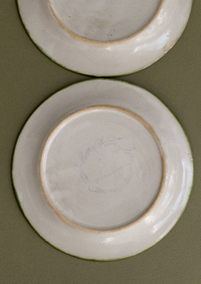A pair of floral and squiggle painted plates in green, blue and orange.