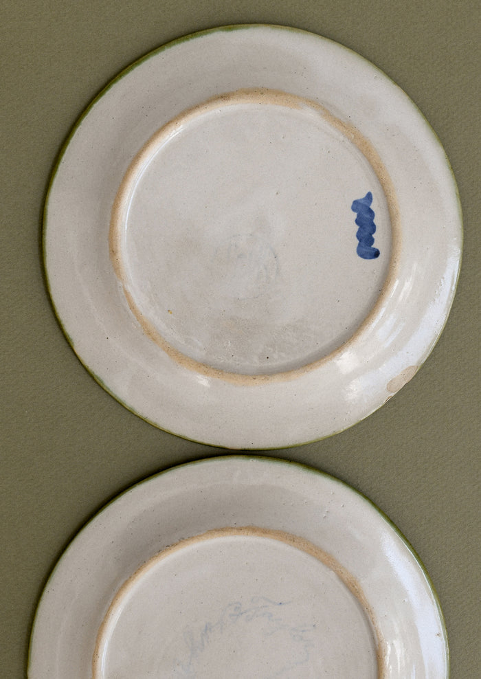 A pair of floral and squiggle painted plates in green, blue and orange.