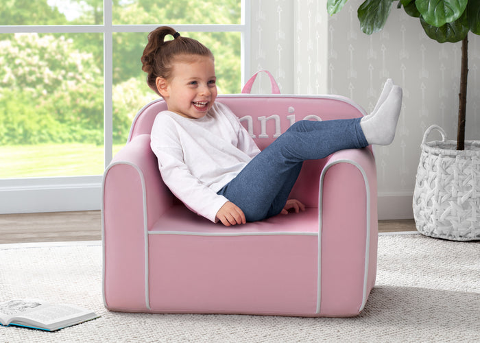 A child sitting on a pink foam chair with the name 'UNICEF' personalized on the backrest.