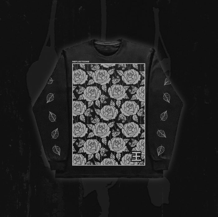 A black Reflections sweatshirt showcases a large white rose pattern on the front with “REFLECTIONS” text across the top, inspired by the ethereal style of Crystal Eyes. White leaf designs adorn both sleeves against a dark background.